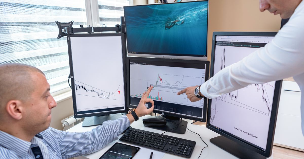 Two business professionals analyzing financial data on multiple computer screens in an office setting.