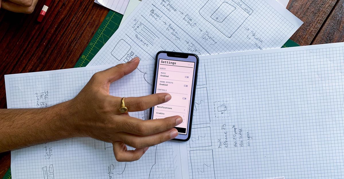 Business Software Solutions Malaysia: Mobile Development Guide for Kuala Lumpur Hand holding smartphone over app design sketches on papers, top view.