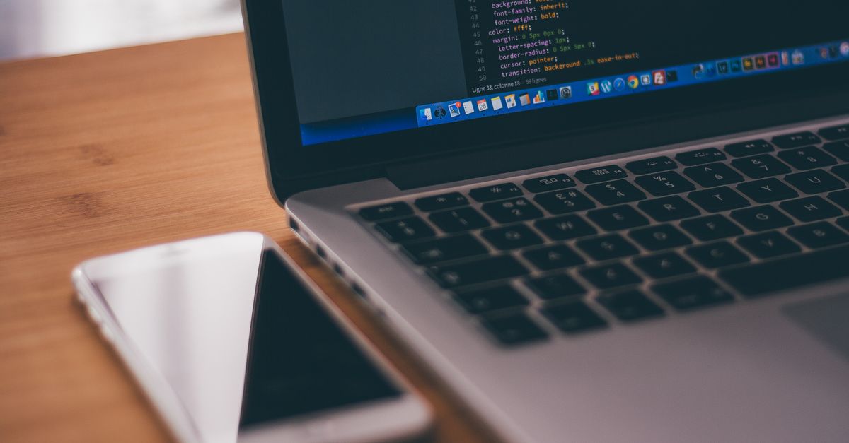 Custom Software Development in Malaysia: Expert Guide for Kuala Lumpur Businesses Coding setup with laptop displaying code and smartphone on a wooden table, ideal for tech themes.