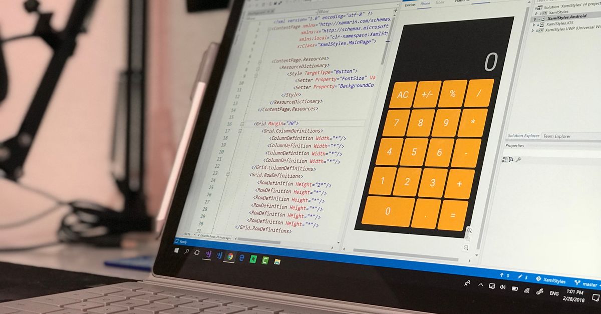 Custom Software & Mobile App Development Services in London, UK – Expert Guide A laptop screen shows a coding application with a calculator design in a tech office setting.