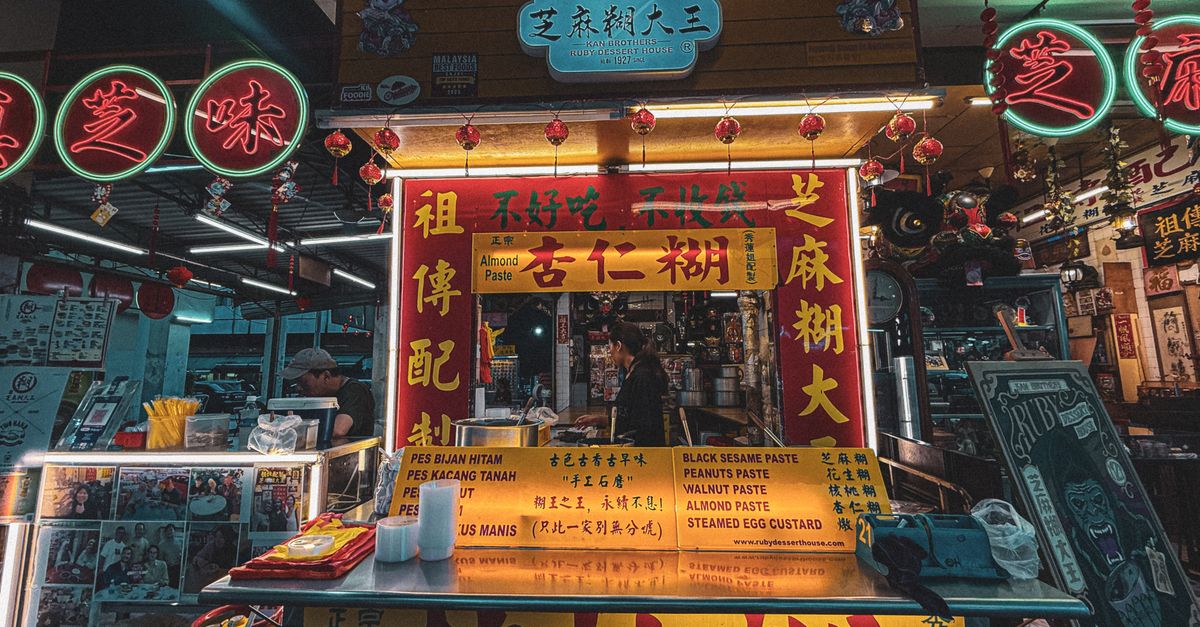 Social Media & Digital Marketing Malaysia: Content That Converts | V Solve Authentic Malaysian street food stall in a Kuala Lumpur market, vibrant signage and lighting.